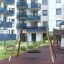 Nestschaukel (BNS 90 cm) auf modernem Spielplatz mit Gummibelag vor Wohngebäude