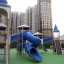 Zitadelle Spielplatz mit blauen Spieltürmen und Spiralrutschen auf grünem Boden vor Hochhauskulisse.