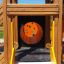 Barrierefreier Spielplatz mit hölzernem Klettergerüst und integriertem Röhrenrutscheneingang.