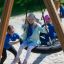 Kinder spielen auf einer Dreifache Schaukel mit Nest-Sitz im Freien.