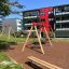 Kinderspielplatz mit Schaukeln aus Lärchenholz und Metall vor modernem Wohngebäude.