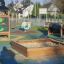 Spielturm mit Drachen-Motiv und Sandkasten auf einem kinderfreundlichen Spielplatz
