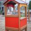 Kind schaut aus einem bunten Spielhaus aus Holz auf einem Spielplatz.