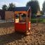 Spielhaus aus Holz auf Spielplatz im Sand, mit roten Wänden und blauem Dach.