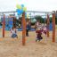 Kinder spielen auf einer Sechseckigen Schaukel aus Robinienholz auf einem Spielplatz.