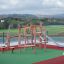 Etna Klettergerüst mit Rutsche auf einem Spielplatz mit grünem Boden und ländlicher Aussicht.