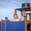 Zwei Kinder spielen auf einem blauen und braunen Spielgerät Dampfer mit Rutsche auf einem Spielplatz