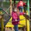 Mädchen in roter Jacke spielt auf einem Spielplatz mit Holzstrukturen.