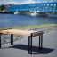 Moderne Thor Tisch aus Holz mit Metallbeinen auf einer Promenade vor einer blauen Brücke