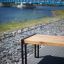 Moderne Thor Bank lang aus Holz und Metall am Flussufer mit blauer Brücke im Hintergrund.