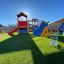 Blauer Jet Federwippe auf einem Spielplatz mit grünem Kunstrasen und einem großen Spielhaus im Hinte