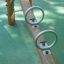 Kinderspielgerät Wippe Robinie aus Holz mit zwei Metallringen auf grünem Untergrund.