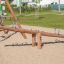 Robuste Wippe Robinie aus Holz auf einem Spielplatz mit Sandboden.