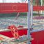 Roter Jupiter Sandkasten mit Lenkrad und Sitzgelegenheiten auf einem Spielplatz.