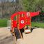 Rotes Spielhaus in Form eines Helikopters mit Rutsche auf einem Spielplatz.