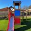 Spielturm mit Klettergerüst, Rutsche und Überdachung auf grünem Rasen.