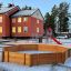 Oktagon Arena I aus Holz auf einem verschneiten Spielplatz neben einem Schulgebäude.
