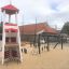 Leuchtturm Spielturm auf einem Spielplatz mit Kletterseilen und Rutsche.
