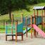 Epsilon Barrierefreie Spielplatz mit Rutsche, Kletterelementen und Brücke aus Holz und bunten Paneel