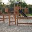 Spielplatz Trimm-dich-Pfade aus Holz mit Klettergerüst und Rutsche im Sandbereich.