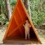 Kind steht in Tipi Spielhaus aus Holz im Wald.