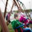 Kinder auf Schaukel 2+2 auf einem Spielplatz, Junge im grünen Pullover und Mädchen in pink.