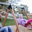 Zwei Kinder lächeln auf Schaukeln im Freien auf einem Spielplatz.