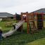 Kinder spielen auf einem Spielplatz mit Rasenmatten, Rutsche und Kletterwand.