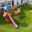 Spielplatz mit Rasenmatten und Holzspielgeräten in einem Außenbereich.