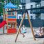 Kinder spielen auf einem Spielplatz mit Logo Spielturm und Vogelnestschaukel BNS 120 cm.
