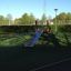 Edelstahl-Hangrutsche auf einem Spielplatz mit grünem Bodenbelag und umgeben von Bäumen