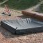 Sandkastenabdeckung 2m x 2m auf einem Spielplatz, graue Schutzhülle über Sandkasten.