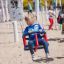 Kind schaukelt auf einem roten und blauen Doppel Schaukel Robinie auf einem Spielplatz.