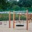Nestschaukel Robinie auf einem Spielplatz mit Sandboden und Klettergerüsten im Hintergrund