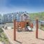 Spielplatz mit Flexischaukel Robinie in einem Sandbereich vor Wohngebäuden.