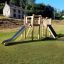 Alstad Spielkombination mit Rutsche Eco aus Holz auf Spielplatz bei Sonnenschein.