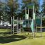 Fort mit zwei Türmen und einer Rutsche aus Metall und grünen Paneelen auf einem Spielplatz.