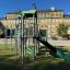 Fort mit zwei Türmen und einer Rutsche aus Metall und Kunststoff in Grün auf einem Spielplatz.