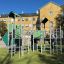Fort mit zwei Türmen und einer Rutsche aus Metall und grünen Paneelen auf einem Spielplatz.