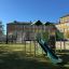 Fort mit zwei Türmen und einer Rutsche aus Metall und Kunststoff auf einem Spielplatz.