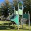 Fort mit zwei Türmen und einer Rutsche aus Metall und grünen Paneelen auf einem Spielplatz.