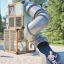 Breezekiste mit Rutsche auf modernem Spielplatz aus Holz und Metall mit Kind, das die Rutsche hinunt