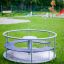 Karussell für Kinder im Freien auf einem Spielplatz, umgeben von Gras und Spielgeräten.