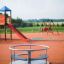 Rundes Karussell auf einem Spielplatz mit weiteren Spielgeräten im Hintergrund.