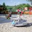 Kinder spielen auf einem Karussell auf einem Spielplatz mit Sandfläche.