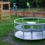 Karussell für Kinder im Freien auf einem Spielplatz, umgeben von Gras und weiteren Spielgeräten.