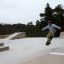 Junger Skateboarder führt einen Sprung auf einer städtischen Skatepark-Rampe aus.