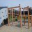 Holzspielplatz Aztek mit Kletterwand und Rutsche in einem Outdoor-Spielbereich.
