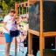 Vater hilft Tochter beim Klettern auf einem Spielplatz mit Klettergerüst mit Kletternetz und Rutsche