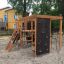 Klettergerüst mit Kletterwand und Rutsche auf einem Spielplatz mit Sandboden.